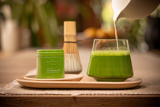 Matcha being poured into a milk cup, chasen (bamboo whisk) in background with YUJO's signature tin